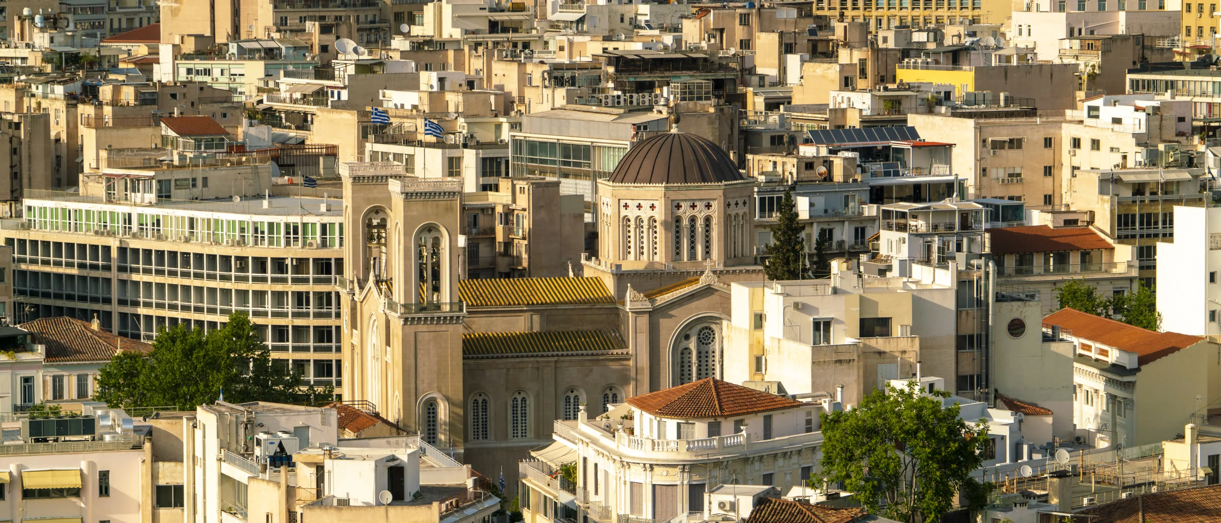 Atina’da yoğun apartman dokusu; ortada kubbeli bir kilise, ikindi ışığı.